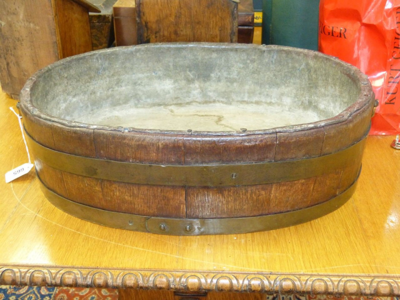 A GEORGE III OAK AND BRASS BANDED WINE COOLER, oval, of coopered construction with a bail handle to each end. 53cm by 39cm