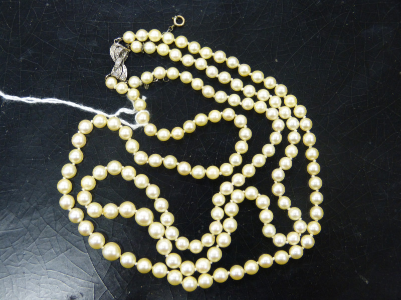 A CULTURED PEARL NECKLACE, the one hundred and fifty graduating cultured pearls all strung knotted into two graduating rows, onto a bow design integral tongue clasp set throughout with eight graduating diamond highlights, and safety chain. Total length ap