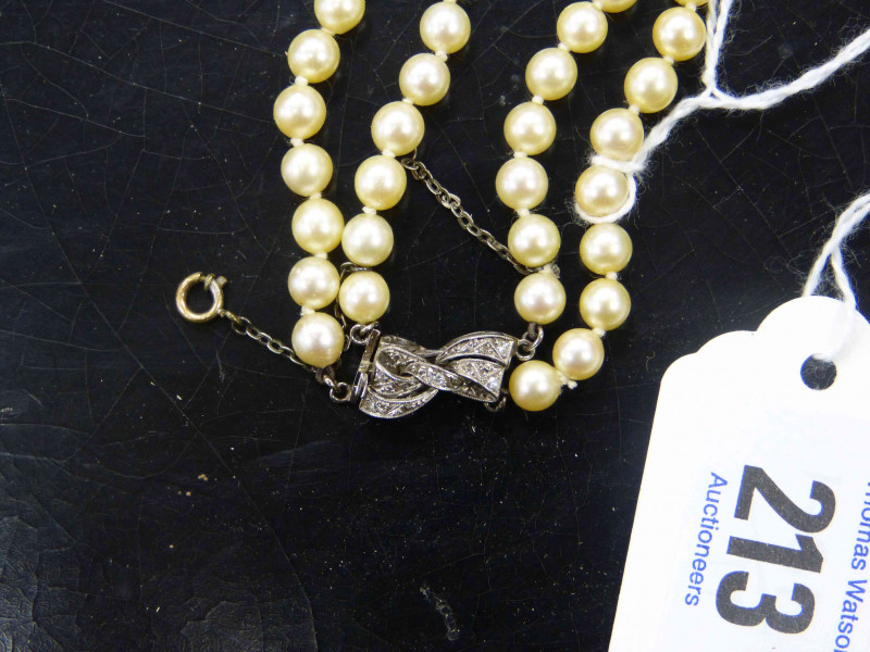A CULTURED PEARL NECKLACE, the one hundred and fifty graduating cultured pearls all strung knotted into two graduating rows, onto a bow design integral tongue clasp set throughout with eight graduating diamond highlights, and safety chain. Total length ap