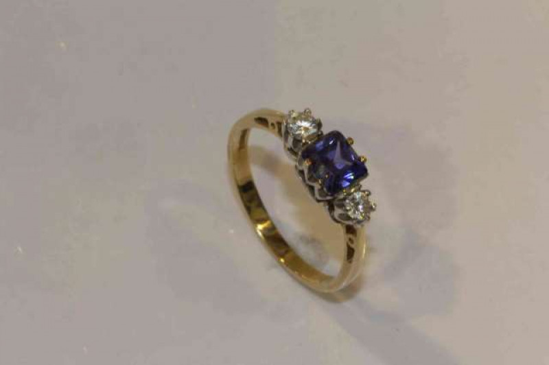 A tanzanite and diamond ring, the square cut tanzanite four claw set between two brilliant cut claw set diamonds, all set in pierced detail mounts between pierced open tapering shoulders on a plain band, ring size N, stamped 375, weight 2gms