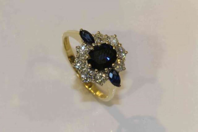 A sapphire and diamond ring, the oval cut sapphire ten claw set raised within a surround of eight brilliant cut claw set diamonds and two marquise cut claw set sapphires, all set in a pierced open mount between solid tapering shoulders on a plain band, st