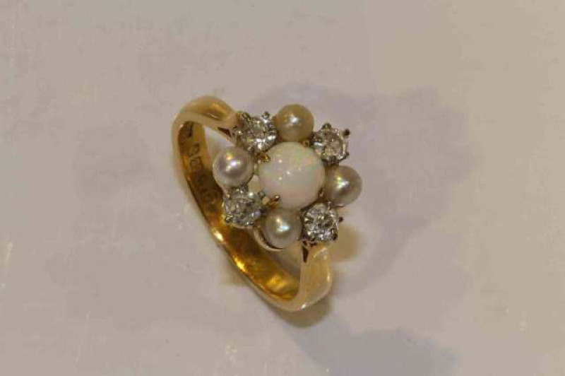 An opal, diamond and seed pearl ring, the round cabochon cut opal four claw set within a surround of four seed pearls alternately spaced with four brilliant cut claw set diamonds, all set in an open mount between pierced tapering shoulders on a plain band