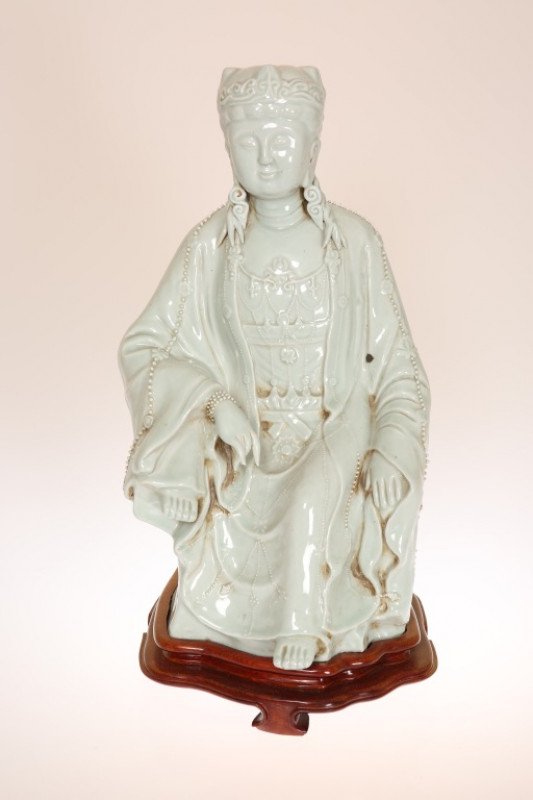 A LARGE CHINESE CELADON GLAZED POTTERY FIGURE OF QUAN YIN, modelled seated with elaborate headdress and jewels, mounted on a hardwood stand. Excluding stand 41cm