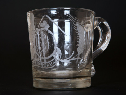 AN EARLY 19TH CENTURY ENGRAVED GLASS 'FARMERS ARMS' CUP, of tapering cylindrical form with scroll handle, engraved with crest, monogram and motto, 'God Speed the Plough'; together with a 'farmers arms' goblet, of similar date, with bucket bowl and knopped thumbnail