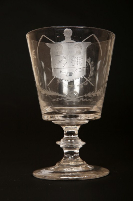 AN EARLY 19TH CENTURY ENGRAVED GLASS 'FARMERS ARMS' CUP, of tapering cylindrical form with scroll handle, engraved with crest, monogram and motto, 'God Speed the Plough'; together with a 'farmers arms' goblet, of similar date, with bucket bowl and knopped
