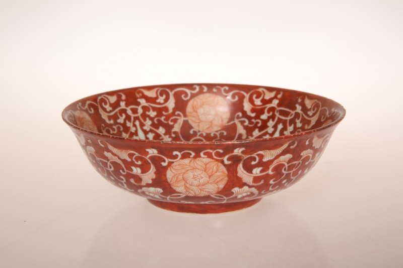 A CHINESE IRON RED REVERSE DECORATED BOWL, decorated with a continuous scrolling foliate lotus and peony design to the exterior and interior, bears six character mark in double circles. 15.5cm