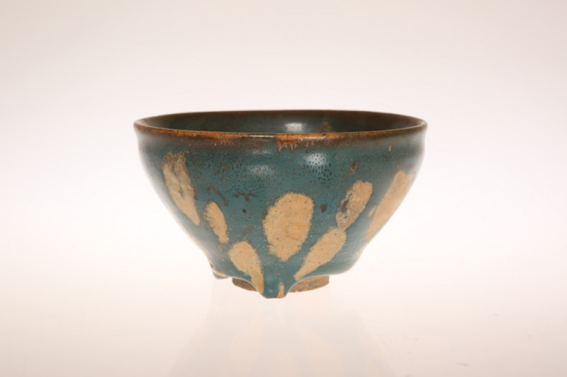 A CHINESE GREEN GLAZED POTTERY BOWL IN THE SUNG STYLE, mottled glazed with unglazed foot. Diameter 11.5cm