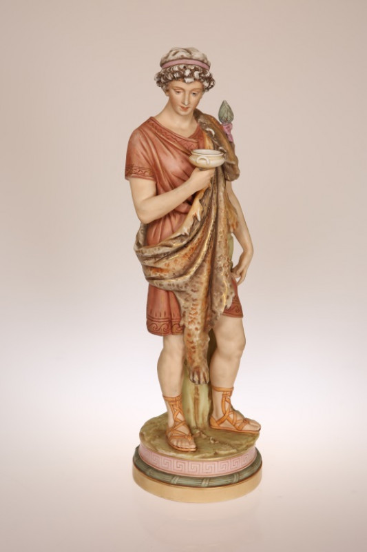 A LARGE ROYAL DUX PORCELAIN FIGURE, c. 1900, of a Roman youth, clad in a lion pelt and holding a wine goblet, in the characteristic palette, pink triangle mark to the base. 51cm