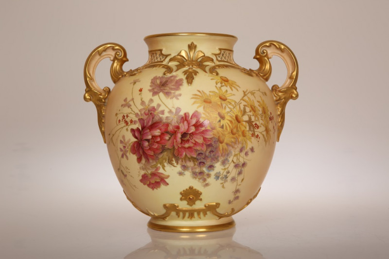 A ROYAL WORCESTER BLUSH IVORY VASE, CIRCA 1896, with twin handles and moulded with scrolls, painted with a floral spray to the front and a smaller spray verso, gilded throughout, shape no. 1515, puce printed factory mark. 22cm