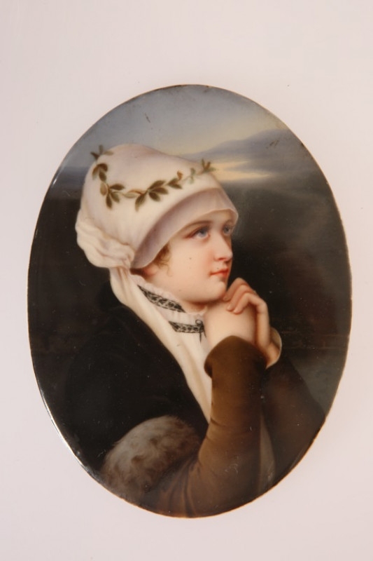 A GERMAN PORCELAIN PLAQUE, LATE 19th CENTURY, oval, painted with a young girl in white bonnet, her hands clasped beneath her chin, impressed numerals verso and indistinctly inscribed in pen. 12cm by 9cm