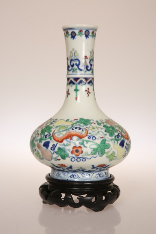 A CHINESE PORCELAIN VASE, of baluster form with elongated neck, painted in polychrome enamels with fruit and bats amidst foliage, the base with blue seal mark, on an ebonised wooden stand. Excluding stand 17cm
