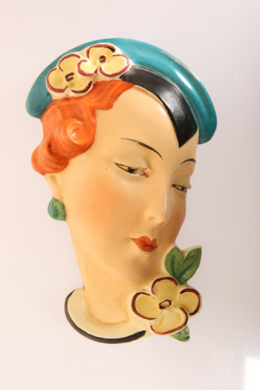 A ROYAL DUX CZECHOSLOVAKIA POTTERY WALL MASK, c. 1930, modelled as a red-headed girl with blue headdress and yellow flowers, impressed no. 15512 and printed mark. 20cm