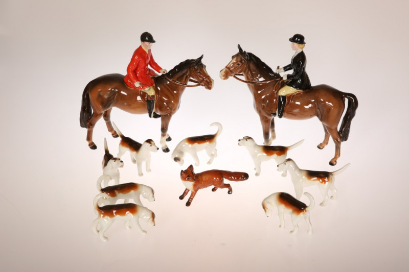 A BESWICK POTTERY HUNTING GROUP, comprising huntsman in a red coat and huntswoman in a black coat, each on a bay horse, with eight hounds and a fox, printed marks. (11) First 18.5cm