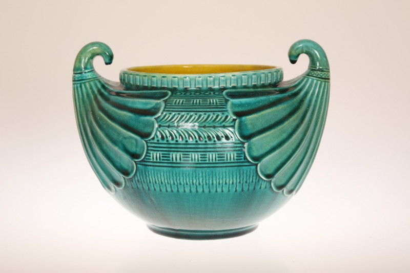 CHRISTOPHER DRESSER (1834-1904) FOR LINTHORPE POTTERY, A JARDINIERE IN THE EGYPTIAN TASTE, green glazed, moulded with twin 'fan' handles and bands of geometric decoration, impressed 2297 to the base. Across handles 26.5cm