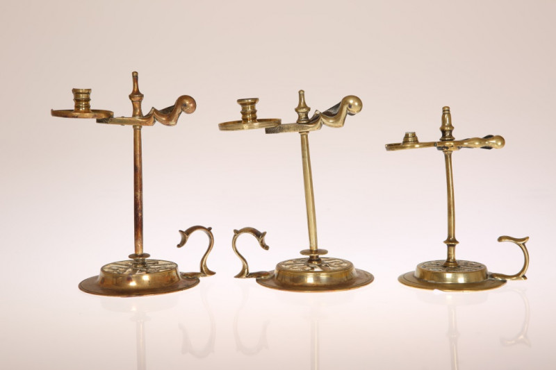 THREE GEORGE III BRASS WAX JACKS, circa 1775, each of characteristic form with urn finial, divided scissor plate, plain stem and on pierced circular foot with scroll thumbpiece. Tallest 15cm