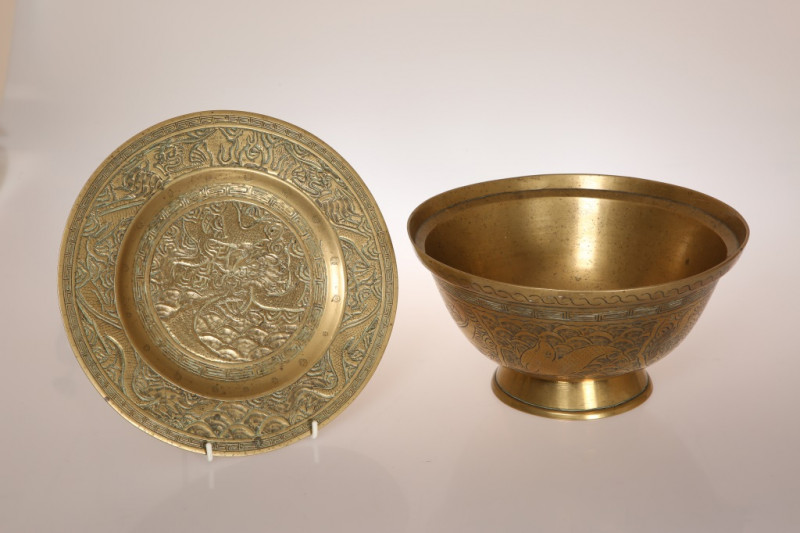 A CHINESE BRASS FOOTED BOWL OR BASIN, with everted rim, the body engraved with bands of Greek Key enclosing a dragon and other creatures, cast seal mark to base, on a plate or stand, similarly decorated and marked. Diameter of bowl 26.25cm