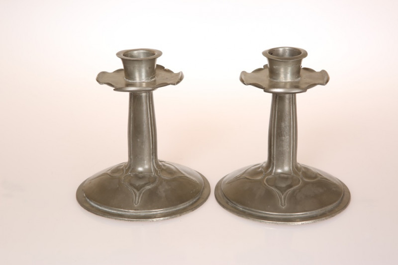 A PAIR OF LIBERTY TUDRIC PEWTER CANDLESTICKS, DESIGNED BY ARCHIBALD KNOX, c. 1900, each with detachable nozzle, scalloped drip pan, tapering stem and circular domed foot with stylised plant-form decoration, stamped marks including no. 023 and Solkets. 14c