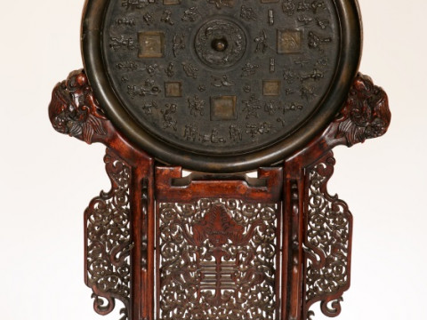 A LARGE CHINESE BRONZE MIRROR IN ARCHAIC STYLE ON A CARVED HARDWOOD STAND,...