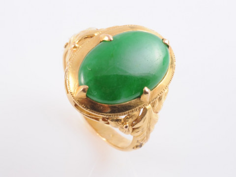 A JADEITE RING, the oval cut jadeite four claw set slightly raised to...