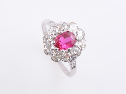 A RUBY AND DIAMOND RING, the cushion cut ruby ten claw set within a surround...