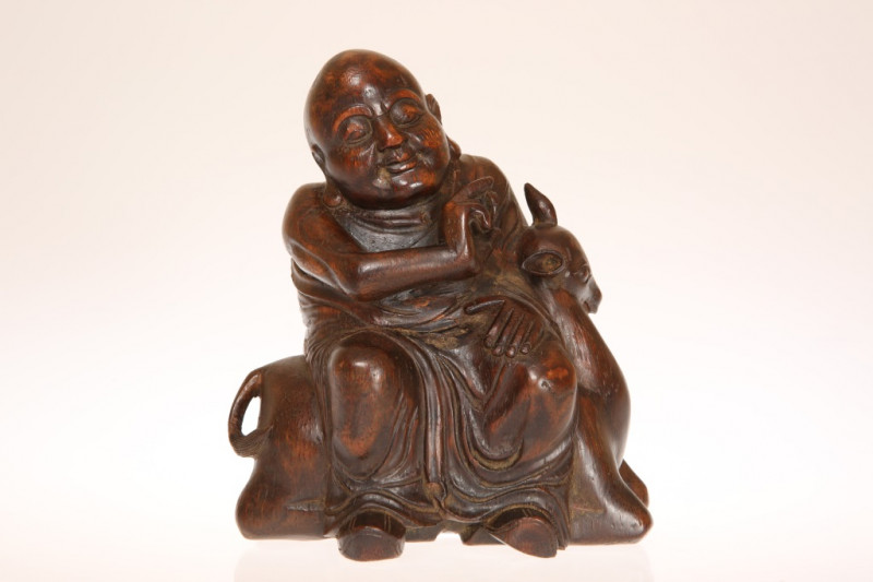 A CHINESE CARVED BAMBOO FIGURE OF A BUDDHA, holding an object in his right hand and seated on a deer. 15cm
