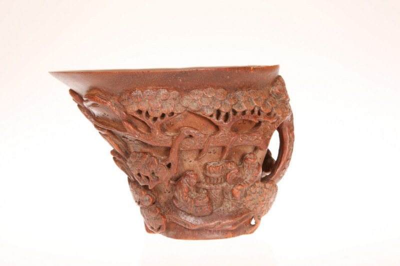 A CHINESE BAMBOO LIBATION CUP, carved in high relief with two figures beneath a spreading pine tree in a mountainous landscape. 10cm by 13.5cm