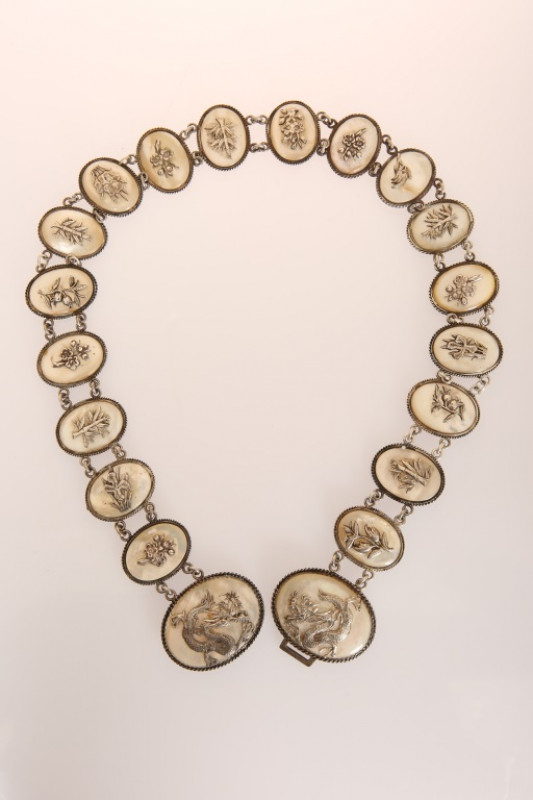 A CHINESE SILVER AND MOTHER-OF-PEARL BELT, CIRCA 1900, with twenty oval links, each with applied silver foliate sprig onto a mother-of-pearl ground, the two larger links forming a buckle and applied with dragons, stamped. 70.5cm long