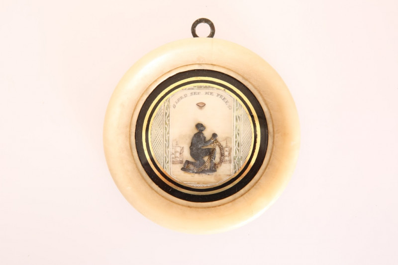 A RARE ANTI-SLAVERY PLAQUE, FIRST QUARTER 19th CENTURY, circular, on ivory, centred by the figure of kneeling slave in chains against a background of ships under the motto 'O Lord Set Me Free', under reverse painted glass with a verre eglomise border and 