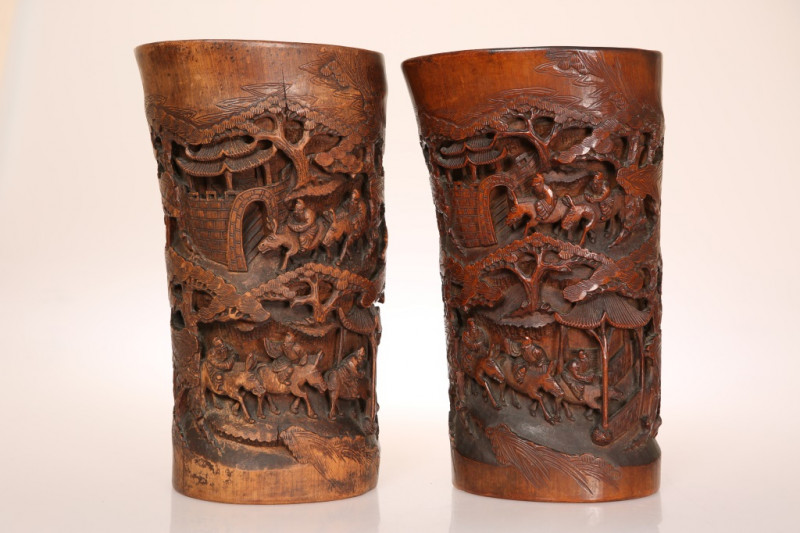 A PAIR OF CHINESE CARVED BAMBOO BRUSH POTS, 19th CENTURY, modelled to resemble tusks, each decorated in high relief with mounted figures in a landscape, rich brown patina. 28cm