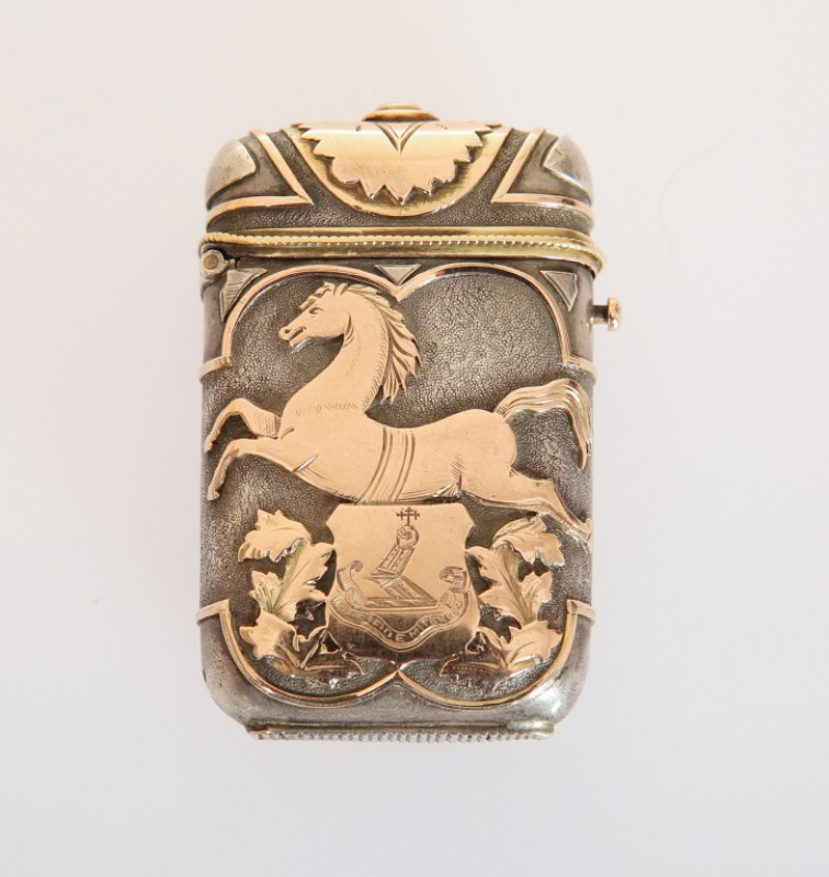 A CONTINENTAL GOLD AND SILVER VESTA CASE, LATE 19TH CENTURY, unmarked, bearing the crest and motto of the Molesworth family, 'Sic Fidem Teneo', opposed by a monogram, the stippled silver ground applied with prancing horses and leaves in yellow gold. Lengt