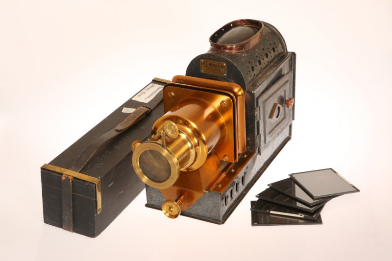 A W.C. HUGHES & CO IRON AND LACQUERED BRASS MAGIC LANTERN, converted to electricity, in a wooden case; together with approximately 320 glass slides, many dating to the early 20th Century, including Venice, Whitby, Gambia, Finland, Zoological Gardens, etc.