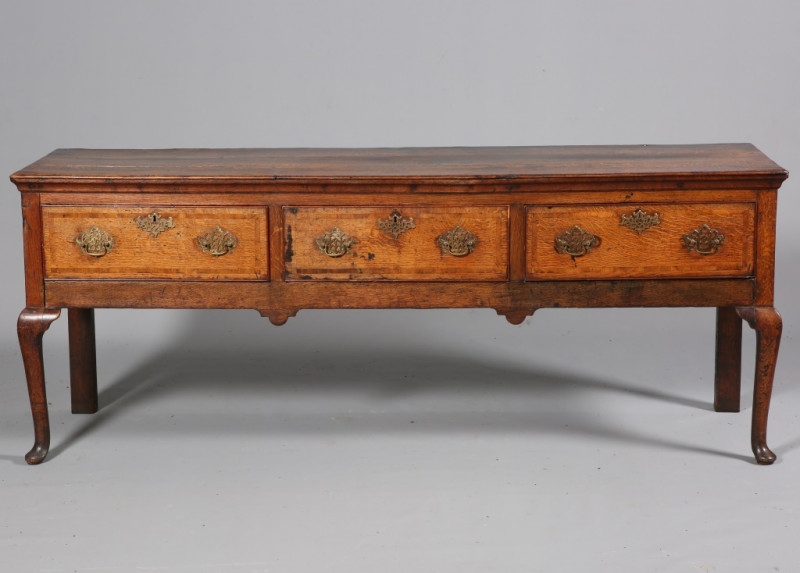 A GEORGE III OAK DRESSER BASE, with moulded rectangular top above three drawers with pierced brass handles and escutcheons and highlighted with banding, raised on cabriole legs. 80cm by 202cm by 51cm