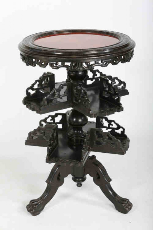 A Chinese carved revolving bookcase table, the circular moulded top enclosing a panel above two four section revolving tiers, raised on a tripod stand terminating in paw feet. 0.81m by 0.52m
