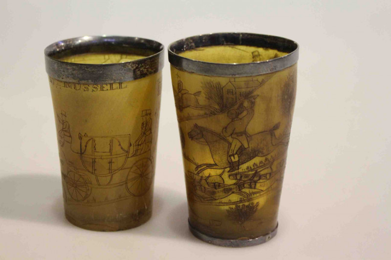 Two antique horn beakers engraved with coaching and hunting scenes, one with hallmarked silver mount