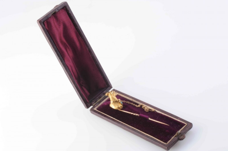 A MID VICTORIAN STICK PIN, modelled as the head of a greyhound with moulded articulated collar set with a single turquoise highlight, with attached safety chain. In fitted case. Length 7cm. Weight 4.9 grams