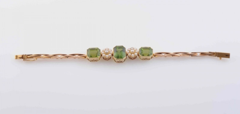 A PERIDOT AND SEED PEARL BRACELET, CIRCA 1900, the central cut-cornered emerald cut peridot collet set between two flower head shaped mounts each set with nine seed pearl highlights, in turn within two further cut-cornered emerald cut peridots, each set o