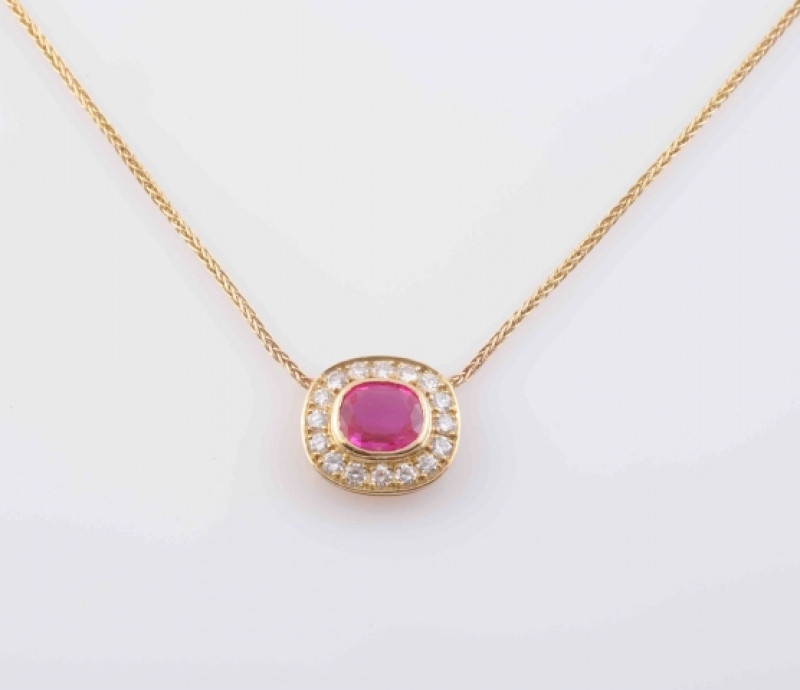 A RUBY AND DIAMOND PENDANT, the oval mixed cut ruby collet set within a surround of sixteen brilliant cut diamonds, suspending from an integral fine snake link chain with bolt ring clasp. Clasp stamped 375. Mount stamped 750. Total length 41cm. Weight 4.3