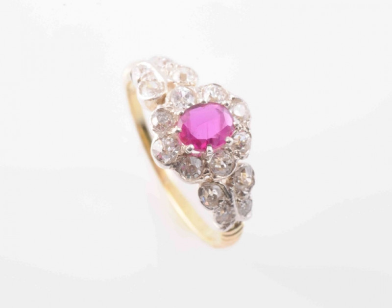 A RUBY AND DIAMOND RING, CIRCA 1900, the oval cut ruby claw set within a scalloped edge surround set with eight old brilliant cut diamonds, between moulded leaf shaped shoulders each set with four graduating old brilliant cut diamond highlights on a mould