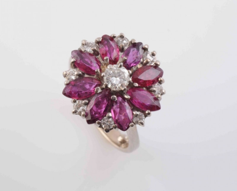 A RUBY AND DIAMOND RING, the central brilliant cut diamond set raised within a surround of eight marquise cut rubies, alternately spaced with eight brilliant cut diamond highlights, all set in a pierced open detail mount between solid tapering shoulders o