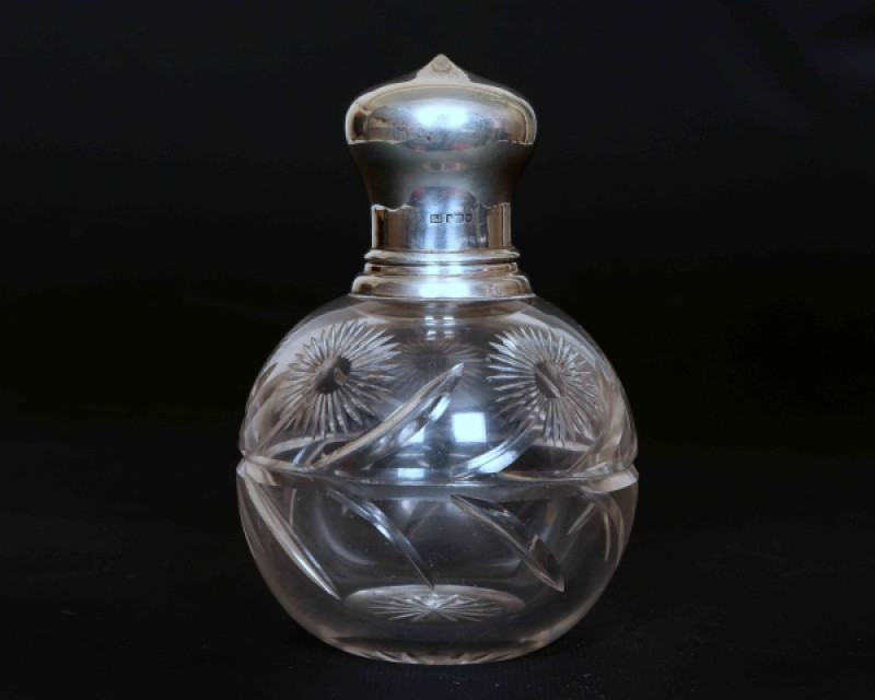 A GEORGE V SILVER-TOPPED CUT-GLASS SCENT BOTTLE, hallmarked for Samuel Jacob, London 1910 (?, date mark indistinct), the lift-off top opening to a glass stopper over a globular body with a band of floral and foliate cutting. 13cm