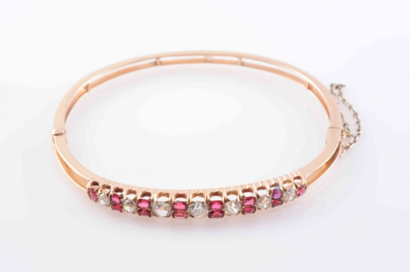 A LATE 19TH CENTURY SPINEL AND DIAMOND BANGLE, the seven graduating brilliant cut diamonds alternately set with six pairs of oval mixed cut spinel highlights and a single further spinel highlight to each end, all set in pierced open mounts in tapering spl