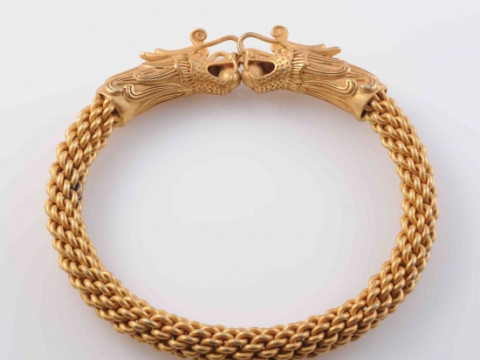 A CHINESE GILT METAL TORQUE BANGLE, the ends elaborately formed to depict...