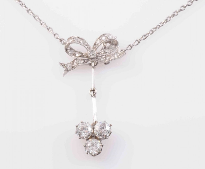 AN EDWARDIAN DIAMOND SET PENDANT, the bow shaped mount set throughout with graduating old brilliant cut diamond highlights, suspending an articulated knife edge bar set to the bottom with three brilliant cut claw set diamonds in a cluster, all suspending 