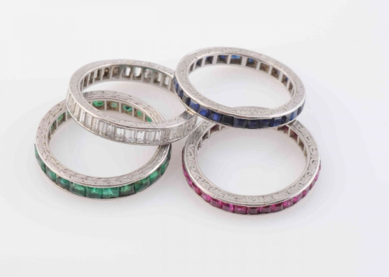 A SET OF FOUR ETERNITY RINGS, to include a ring set throughout with baguette cut diamonds. The second throughout with square cut rubies. The third set throughout with square cut sapphires; and the fourth set throughout with square cut emeralds. Total weig