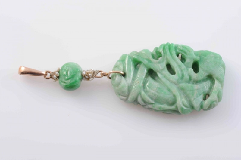 A CHINESE JADEITE PENDANT, the heavily carved large oval jadeite plaque suspending from a further carved jadeite bead to the bottom of an oval pendant loop. Length 7.5cm. Weight 18.6 grams.