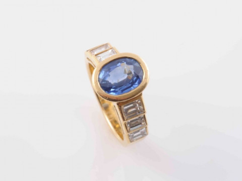 A CONTEMPORARY SAPPHIRE AND DIAMOND RING, the oval cut collet set sapphire...