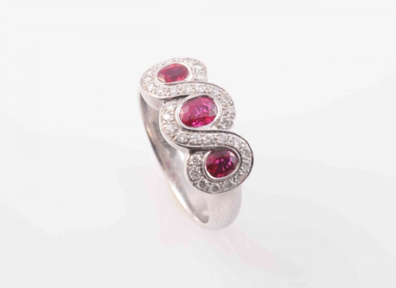 A BURMESE RUBY AND DIAMOND RING, the three oval cut graduating rubies set within a triple figure of eight style mount set throughout with thirty-two brilliant cut graduating diamond highlights, between solid tapering shoulders on a tapering band. Stamped 