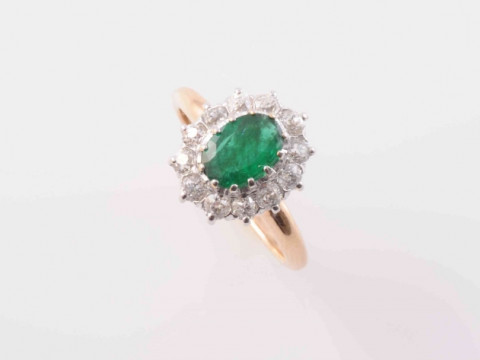 AN EMERALD AND DIAMOND RING, the oval cut emerald twelve claw set within...