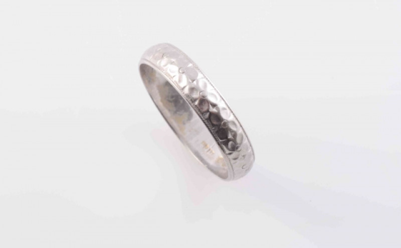 A DIAMOND RING, the single brilliant cut diamond four claw set in a heavy square shaped mount between solid moulded tapering shoulders on a plain band. Ring size M½; AND A WHITE METAL RING, the curved band with engraved floral detailing to the entirety. R