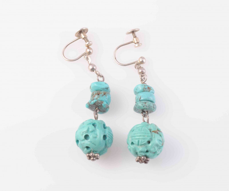 A PAIR OF TURQUOISE EARRINGS, the carved turquoise bead suspending on an articulated link from three further graduating turquoise discs, in turn suspending on an articulated link from shepherd's hook fittings. Fittings stamped silver. Total weight 10.1gms